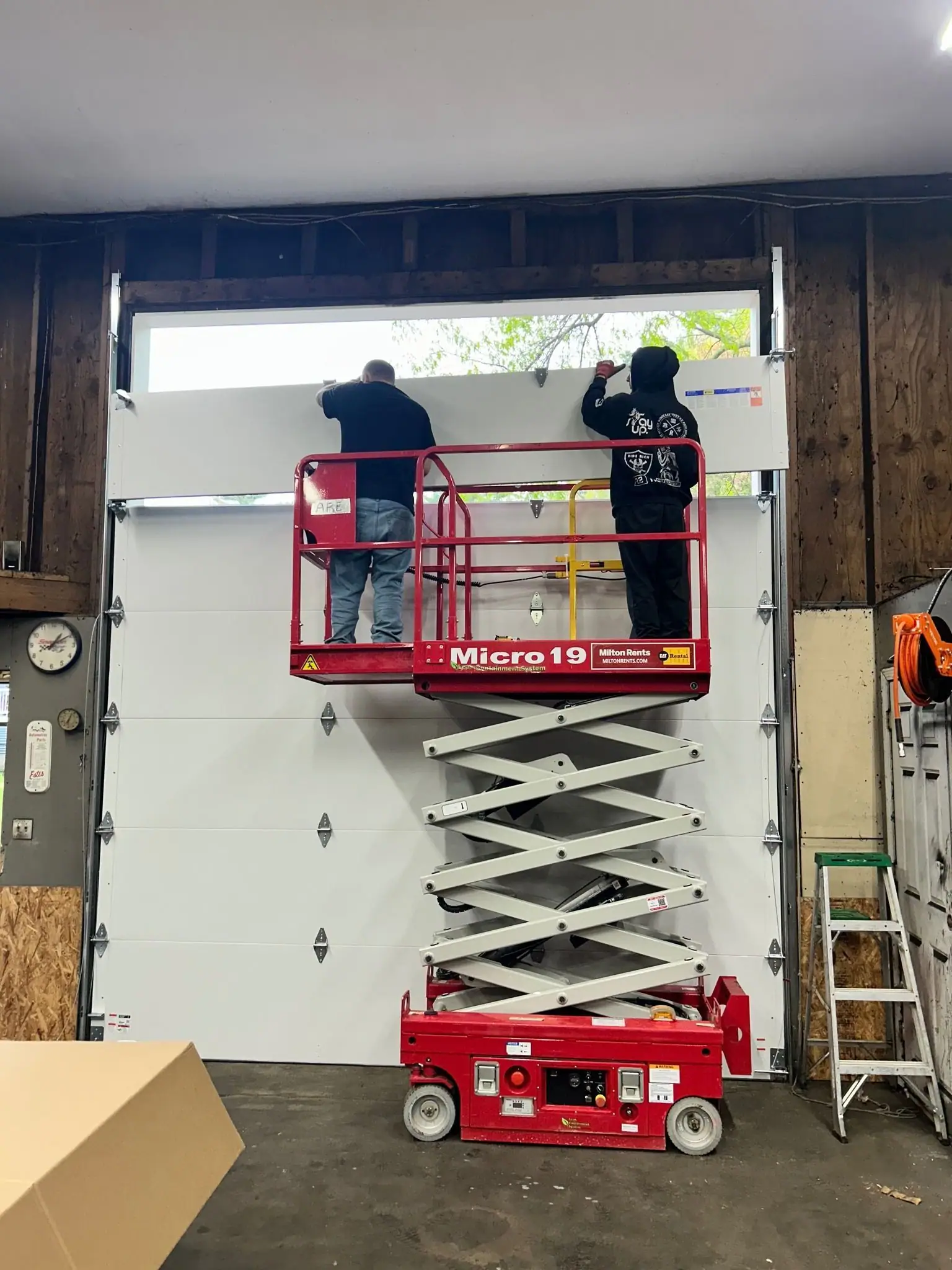 Two installers fitting an overhead door from a scissor lift