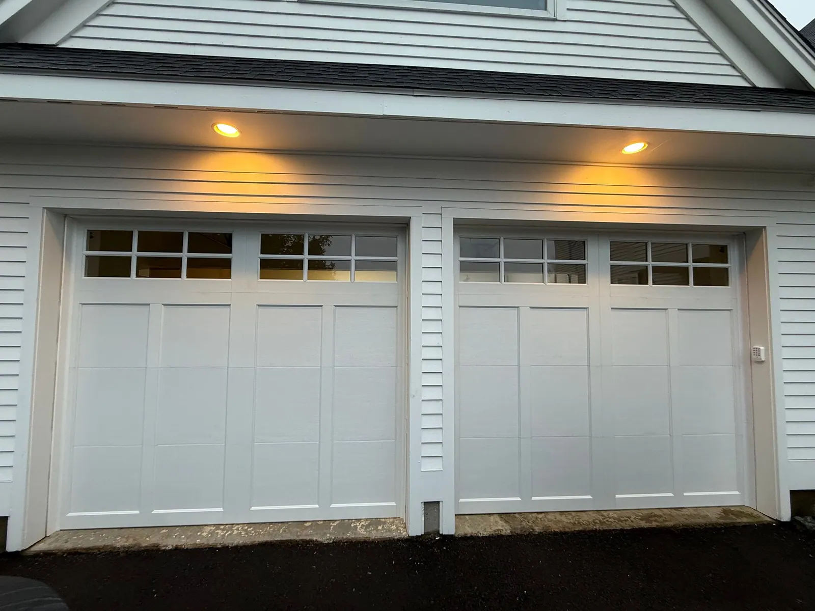 Two white carriage-style garage doors with windows and exterior lighting